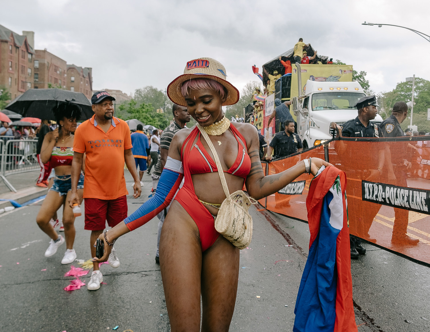 A woman at the West Indian Day Parade wears a colorful bathing suit and a brimmed hat that says &quot;Haiti&quot; with other paradegoers and police officers behind her