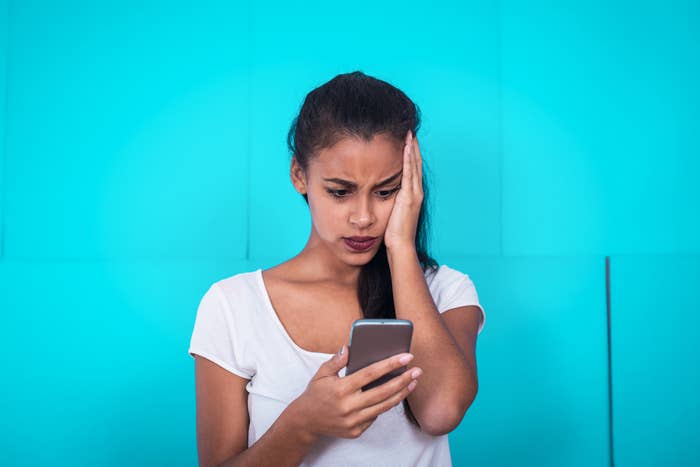 A woman looks at her phone with her hand on face