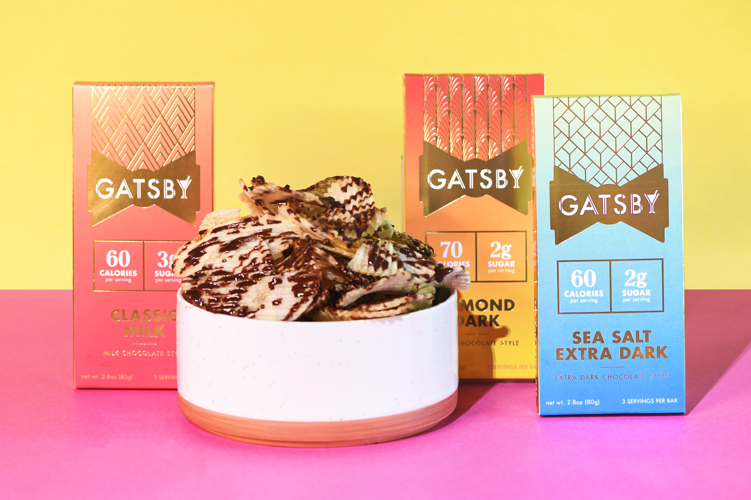 The Almond Dark, Classic Milk, and Sea Salt Extra Dark Gatsby bars next to a bowl of potato chips drizzled with chocolate