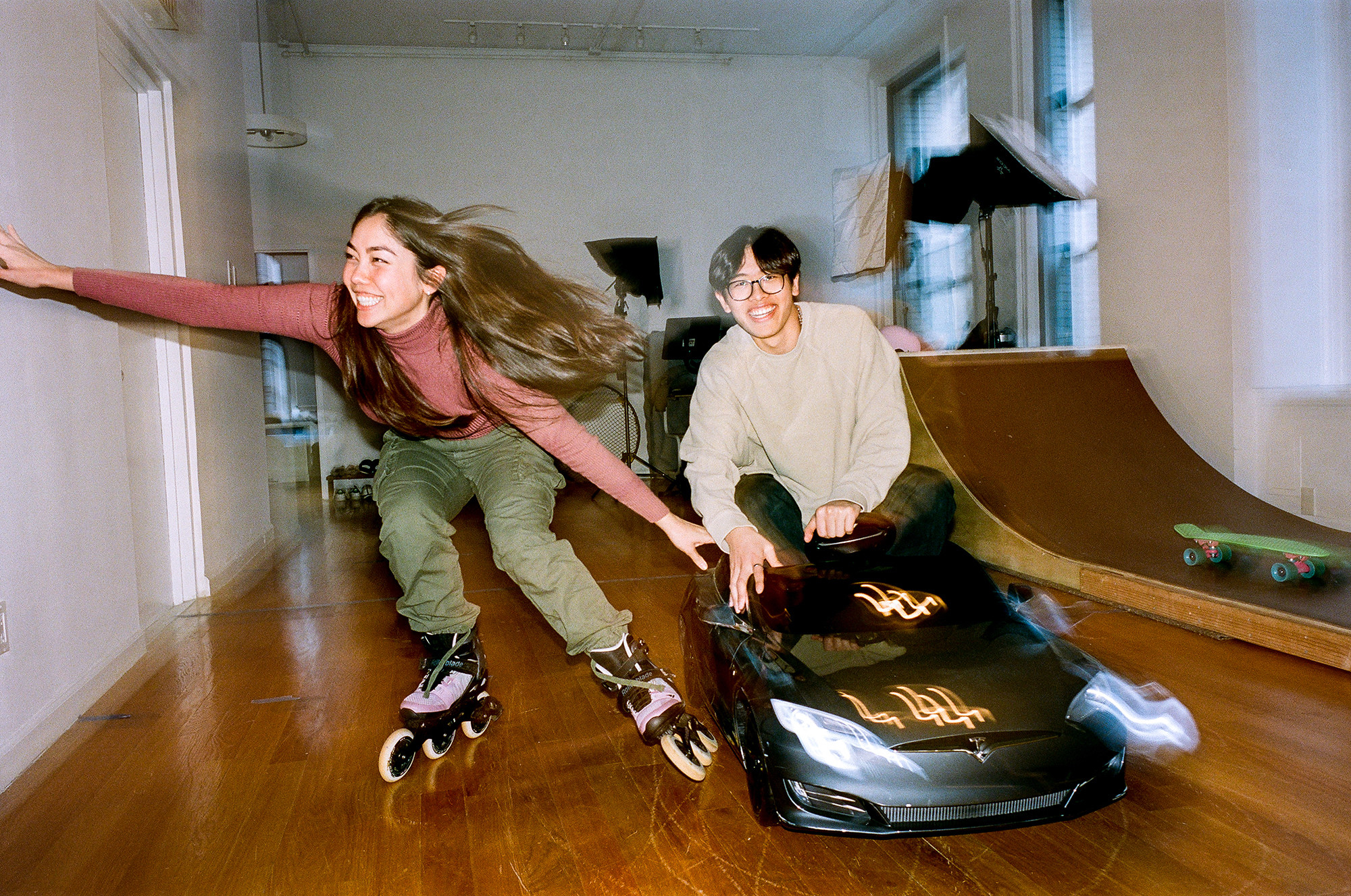 A smiling Annemarie on roller skates and Elliot in a toy car