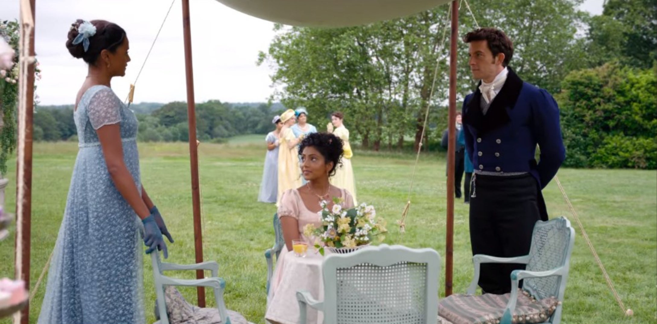 Kate Sharma and Anthony Bridgerton standing up while Edwina Sharma is sitting down looking at Kate.