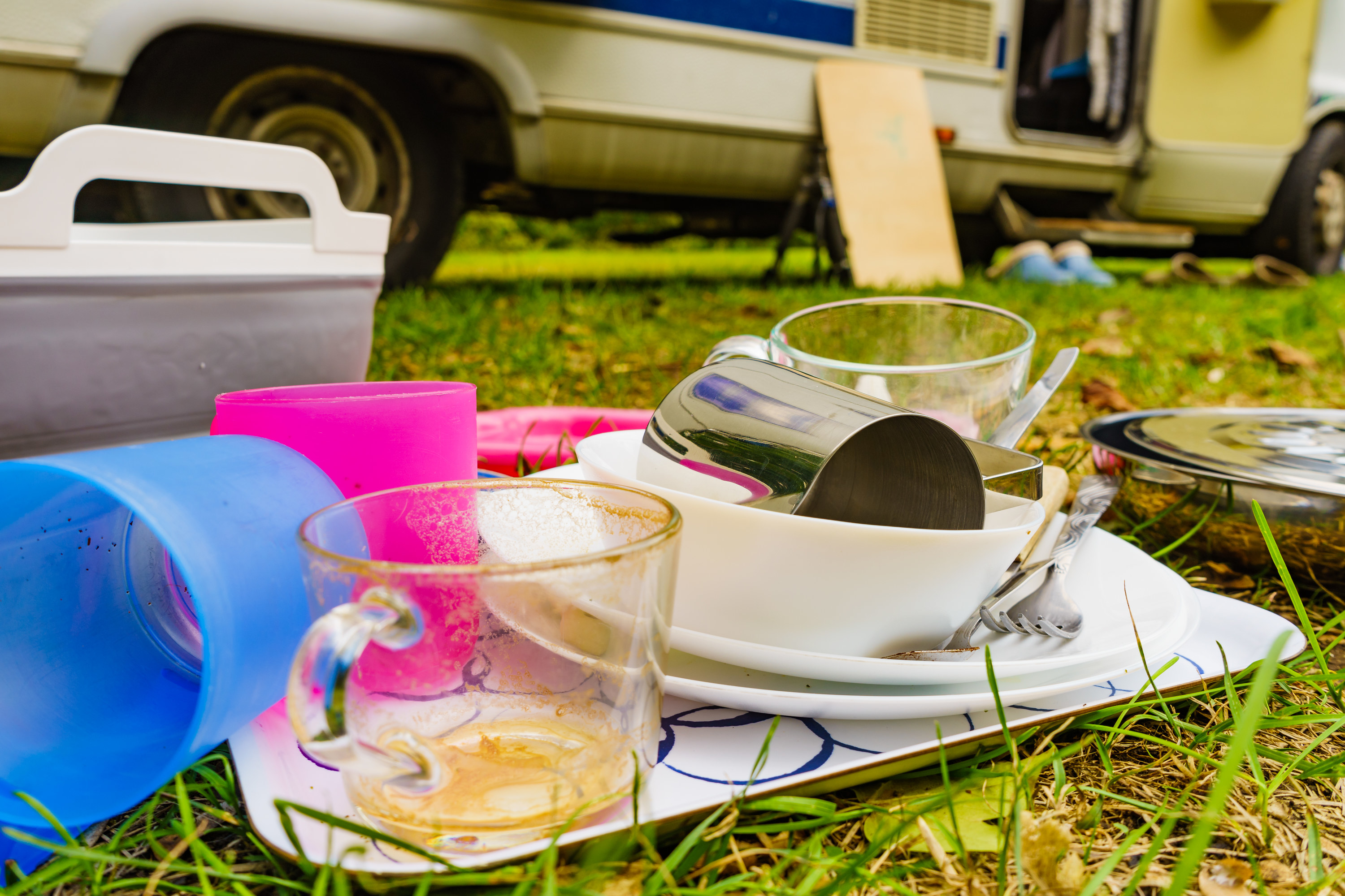 Dirty dishes outdoor against camper vehicle. Washing up on fresh air. Adventure, camping on nature, dishwashing outside