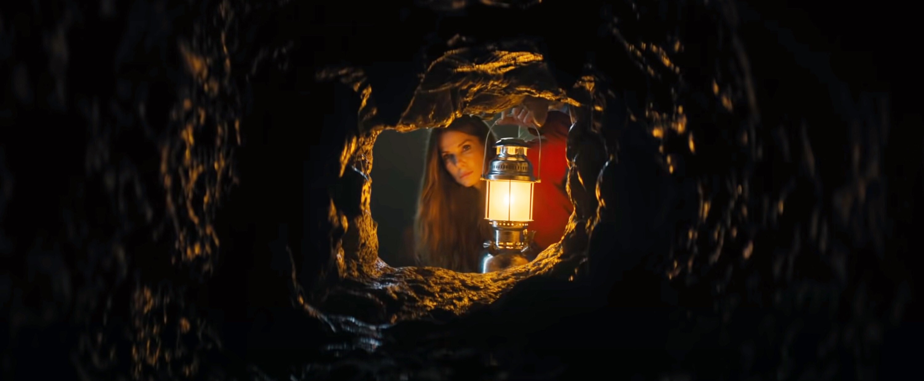 Sandra Bullock holding a lantern up to look through a tunnel in The Lost City
