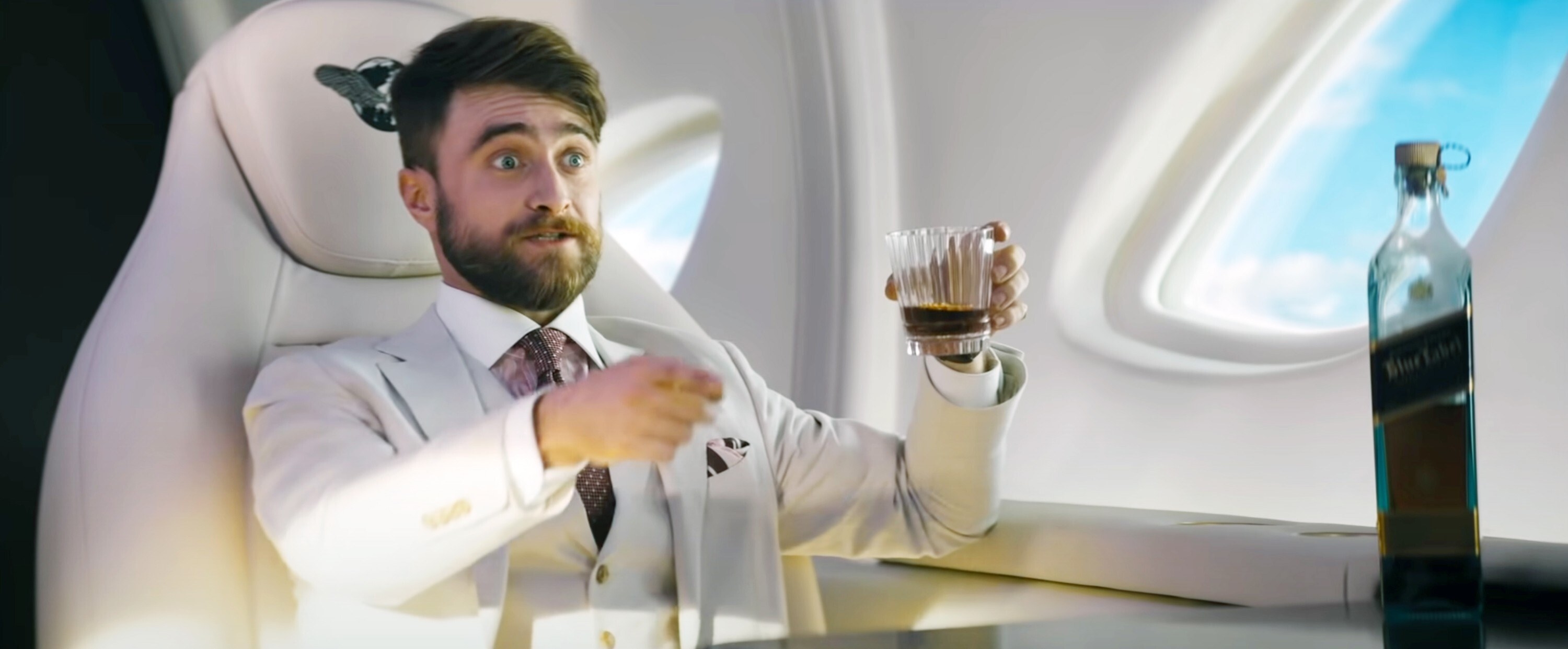 Daniel Radcliffe with a glass of whiskey on a private jet in The Lost City