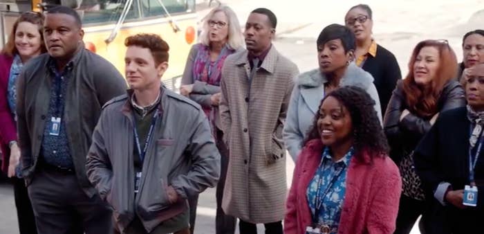 A screenshot from the pilot of the show, showing a group of eleven staff members (mostly teachers) from Abbott Elementary standing outside in front of a school bus.