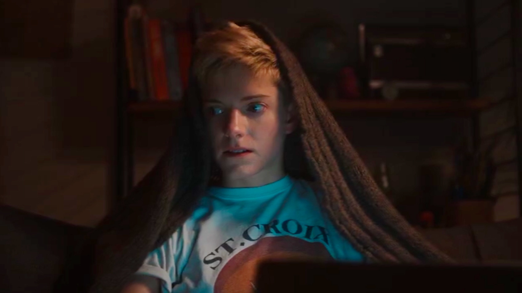 This screenshot from the shows first season shows main character Mae in front of their laptop, looking to the side with a brown blanket over their head, their short blonde hair sticking out over it. Their mouth is slightly open and they look anxious.