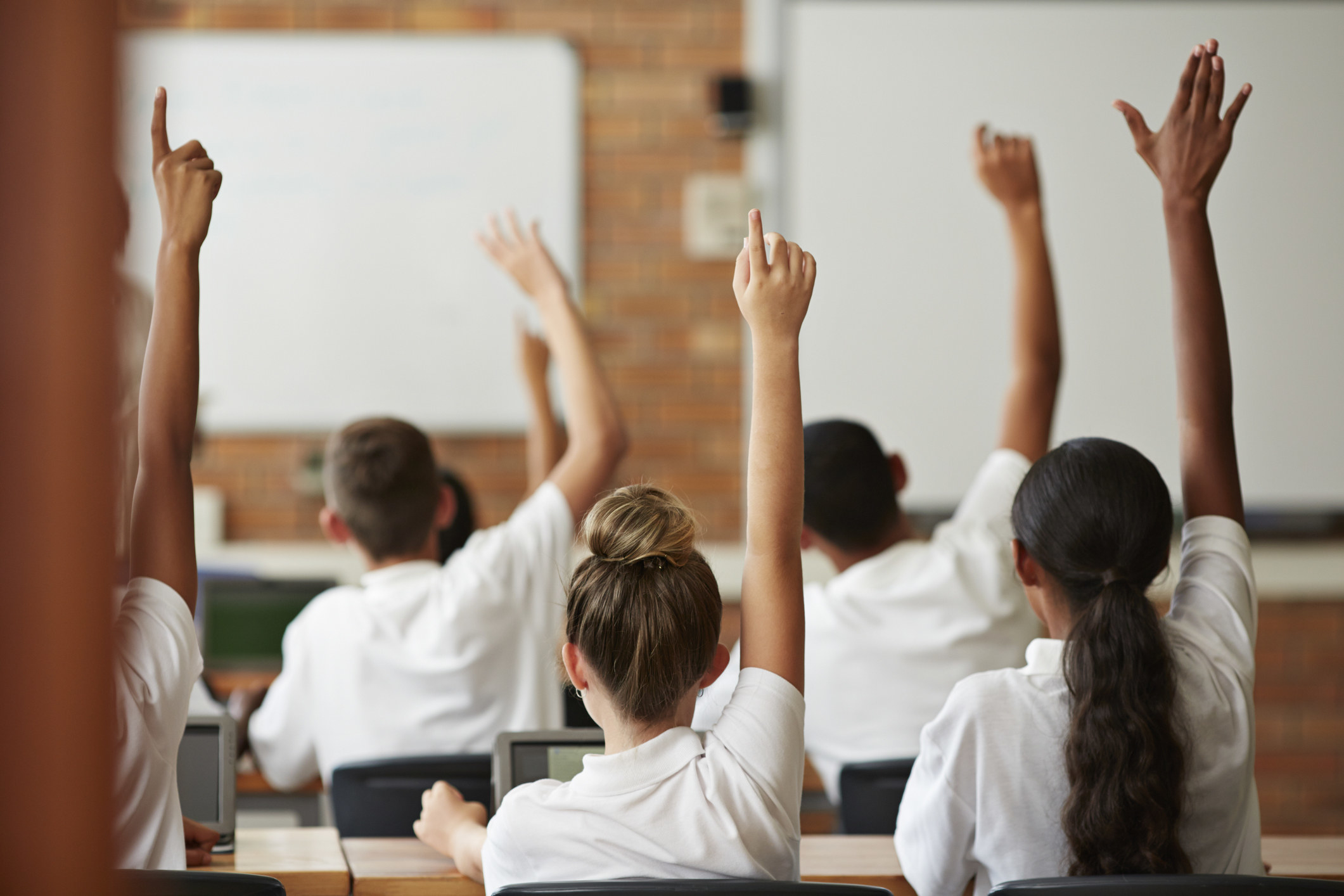 A classroom of kids raising their hands