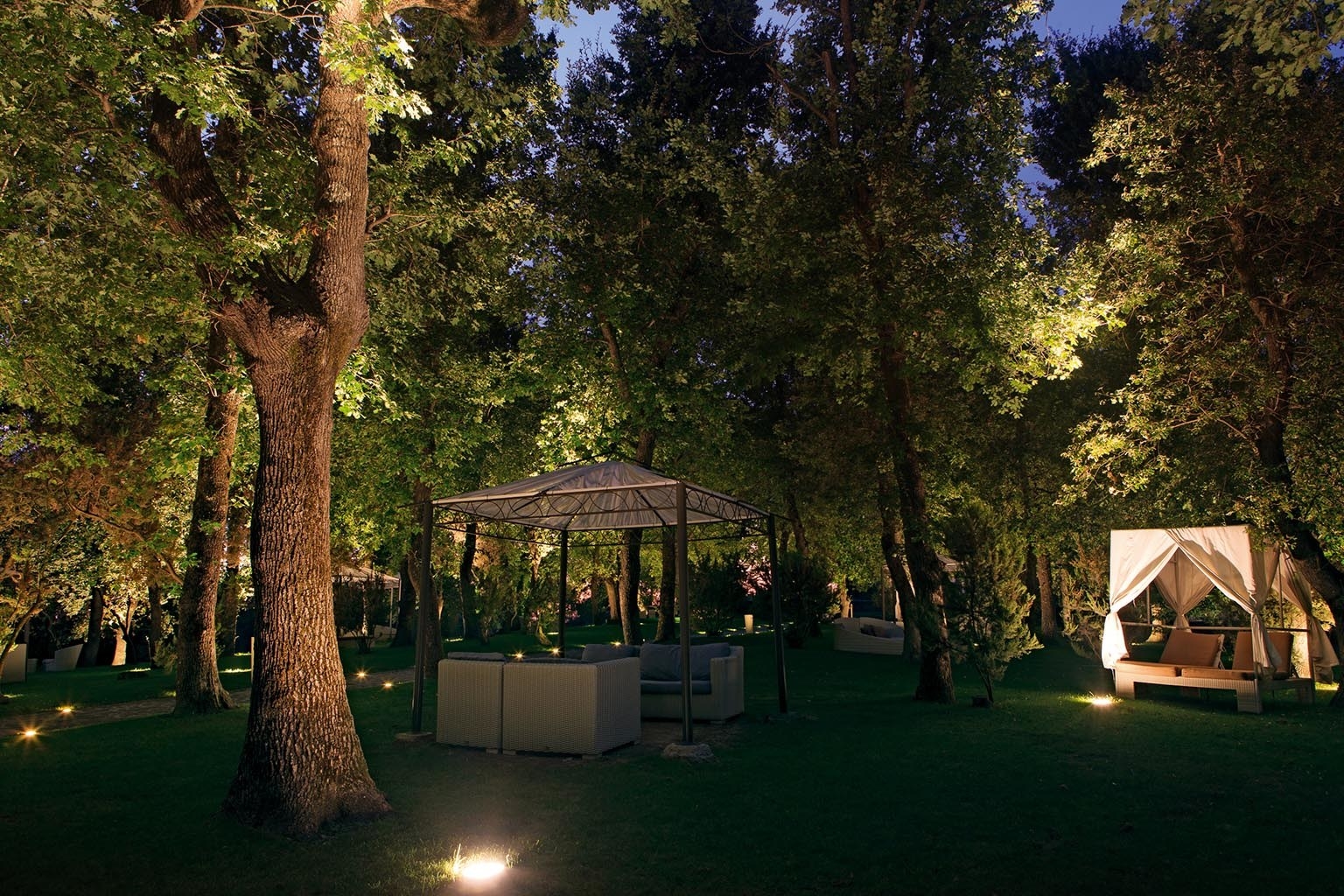 Small cabanas set up among the trees on a grassy lawn at the resort, lit up at night