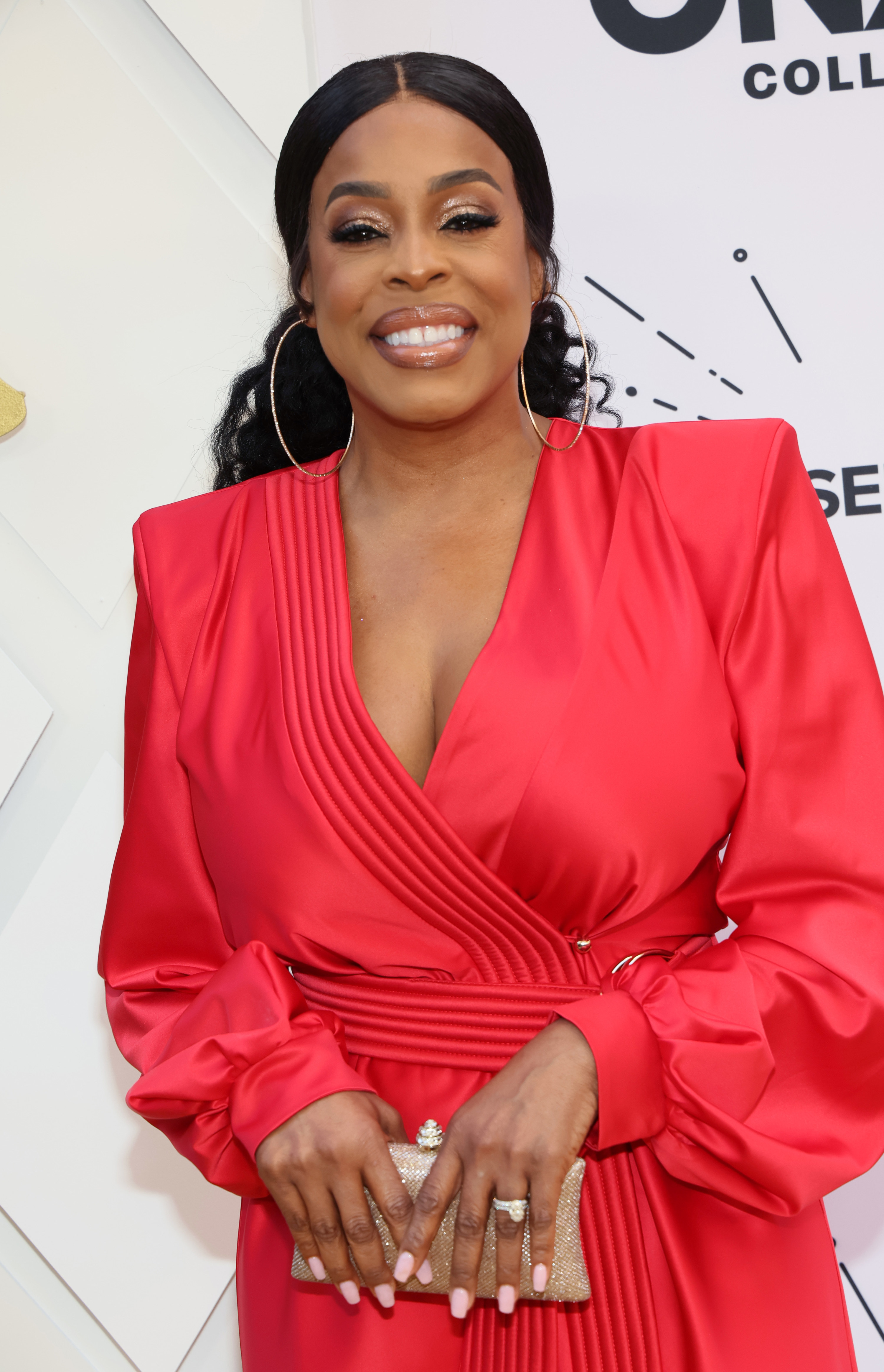 Niecy Nash wearing a long sleeved dress and holding a small clutch at an event