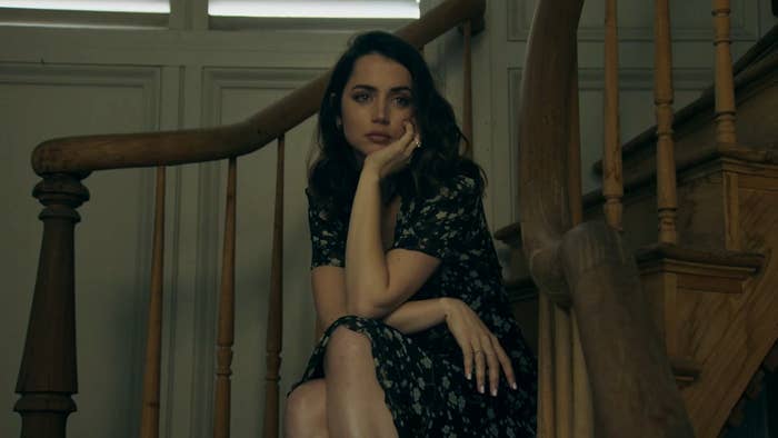 Ana de Armas sits at the bottom of stairs and rests her chin on her left palm and thinks something