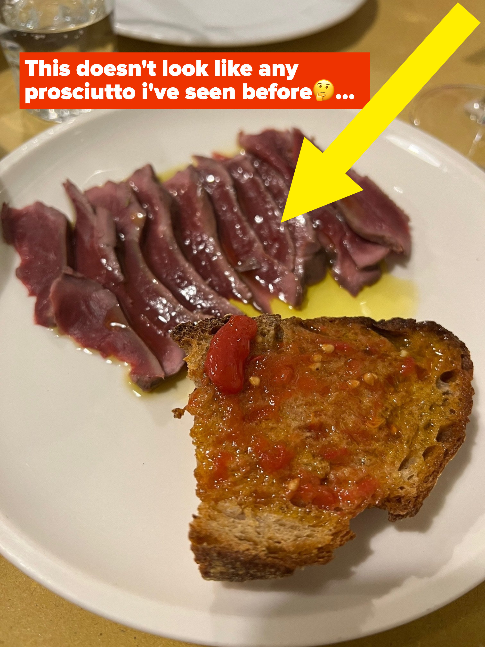 A plate with a slice of bread and cured meat.
