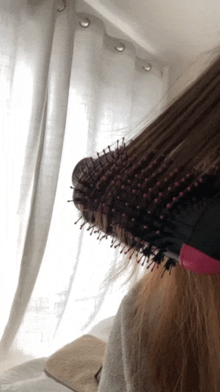 a gif of a buzzfeed writer using the revlon blow dryer brush