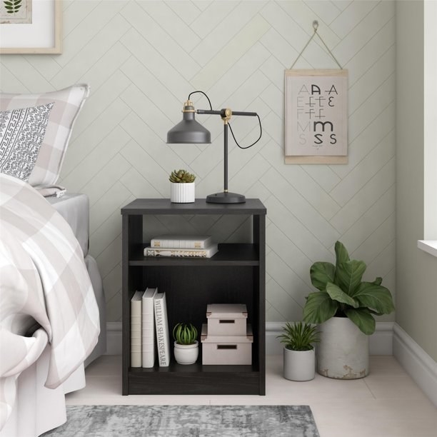 the brown nightstand with books in it and a lamp on the top