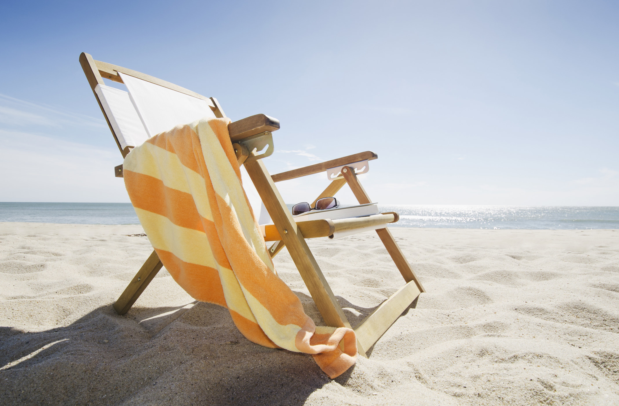 An empty beach chair with a towel draped over the arm