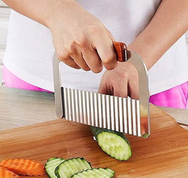A person using the crinkle cutter on a cucumber on a wooden board
