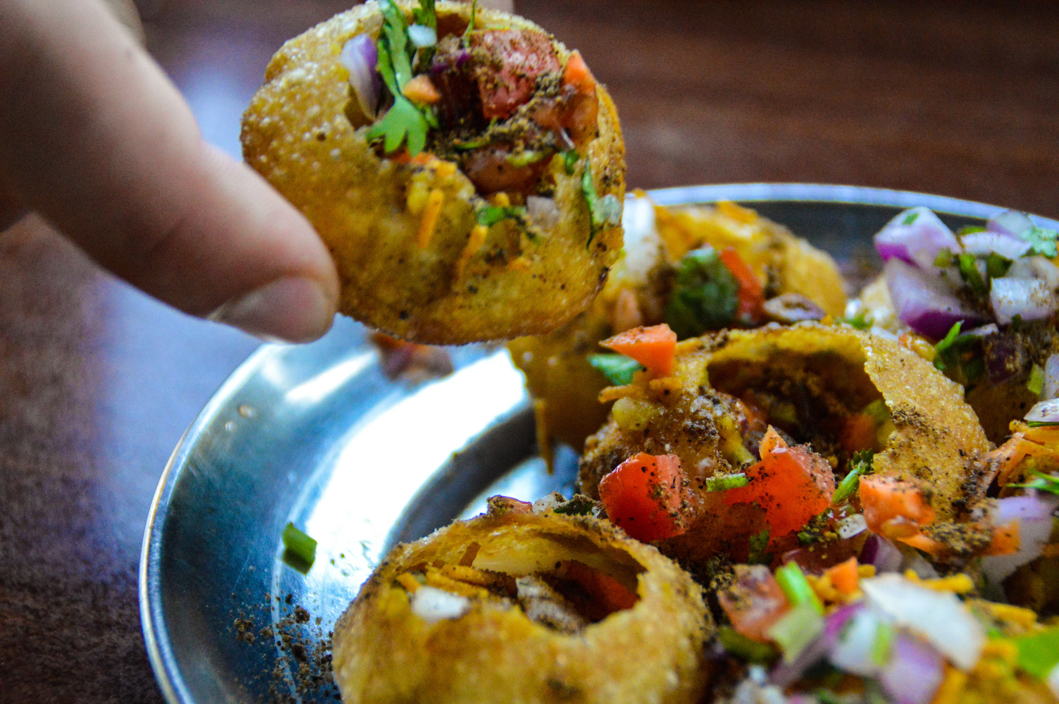 A hand grabbing pani puri from a plate.