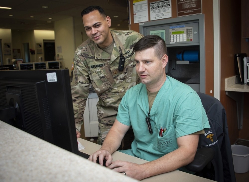 A person with an Army uniform working with a person in scrubs at a computer