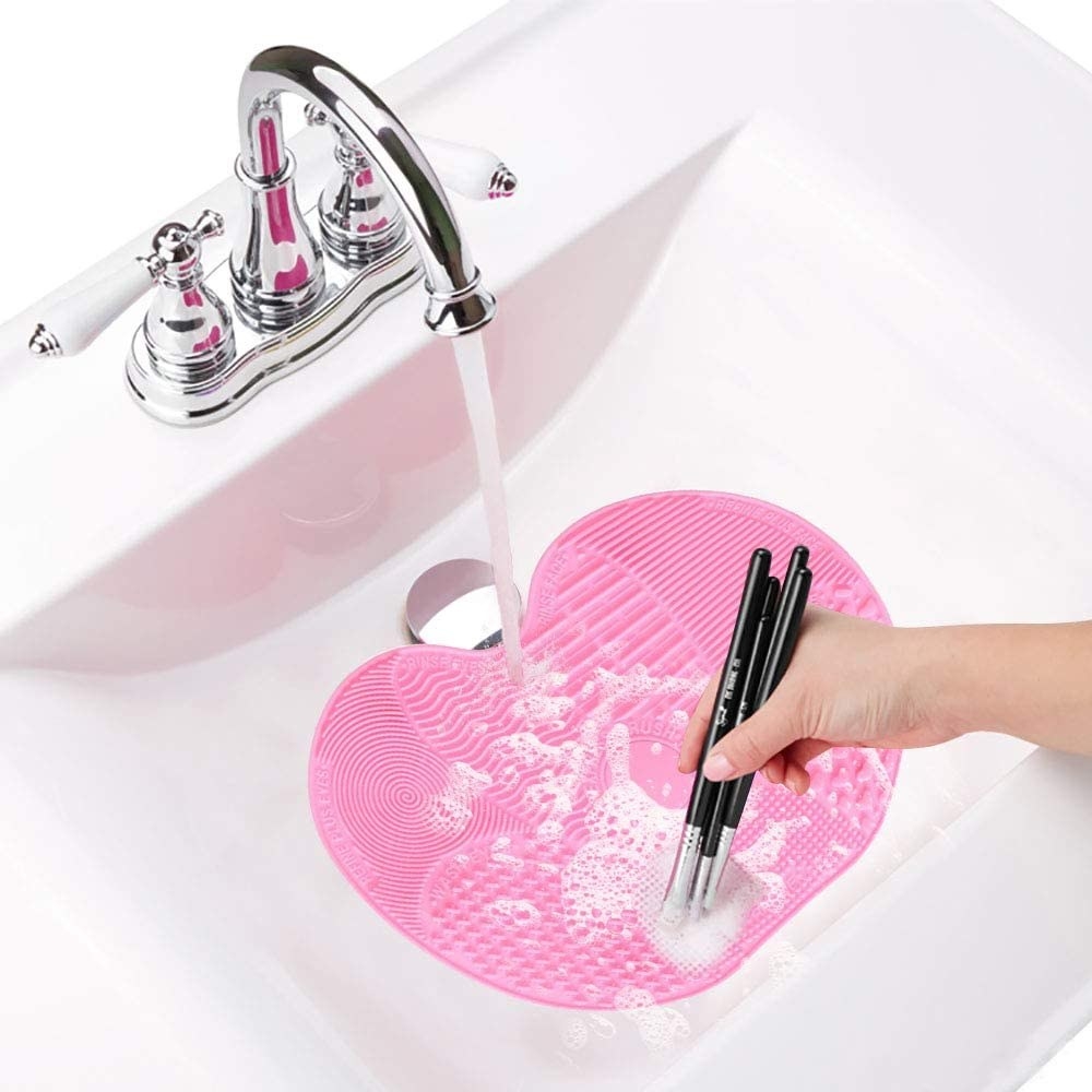 A person washing some makeup brushes on the mat while it sits in their sink