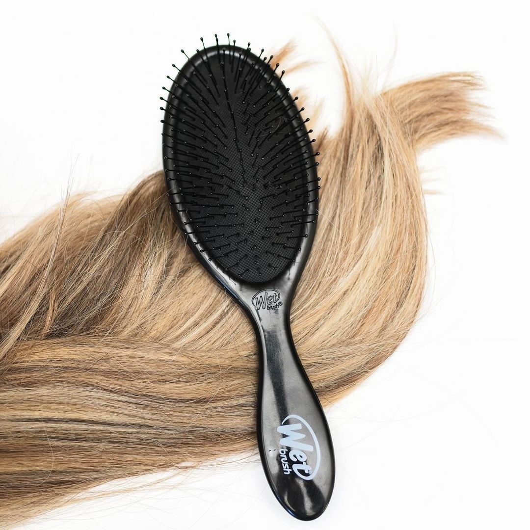 the wet brush in black over a lock of dirty blonde hair