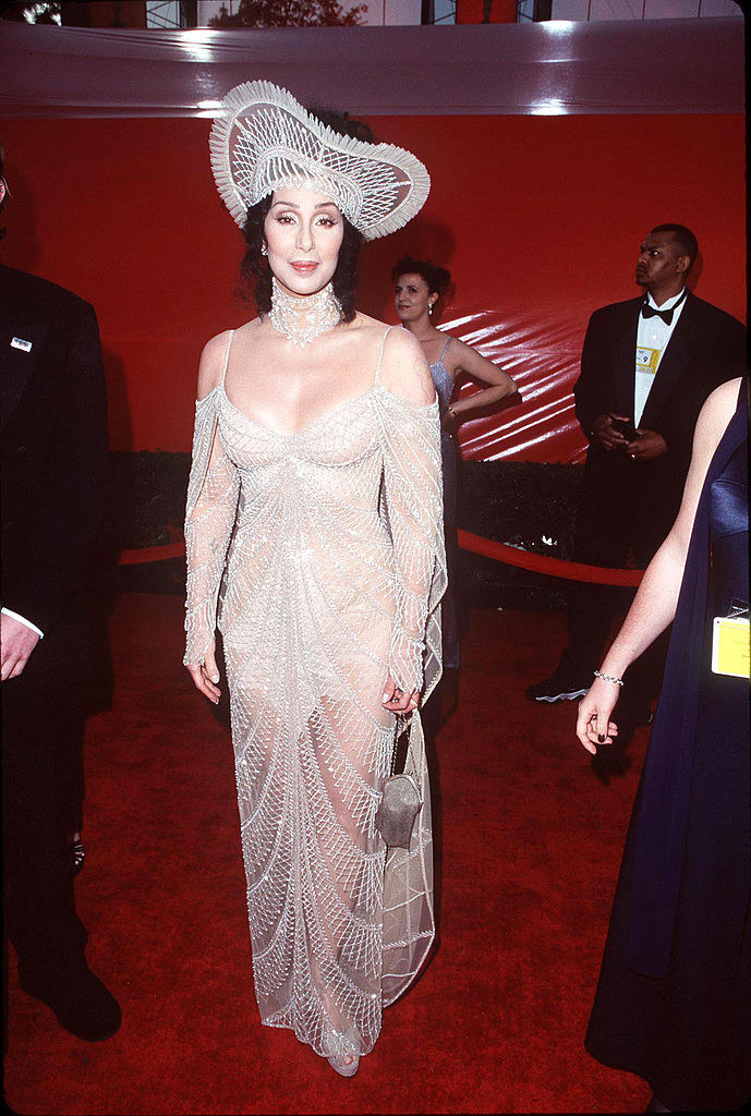 Cher wearing a tight silver beaded gown with a huge hat