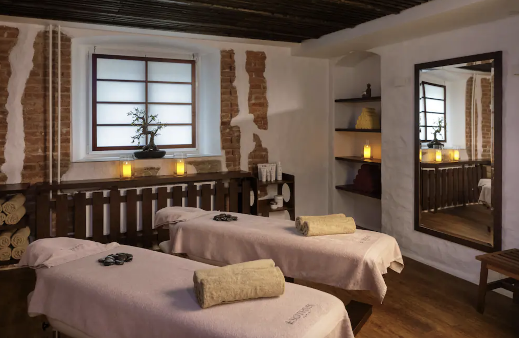 A cozy spa room lit by candles and featuring historic-looking wood ceilings and exposed brick walls