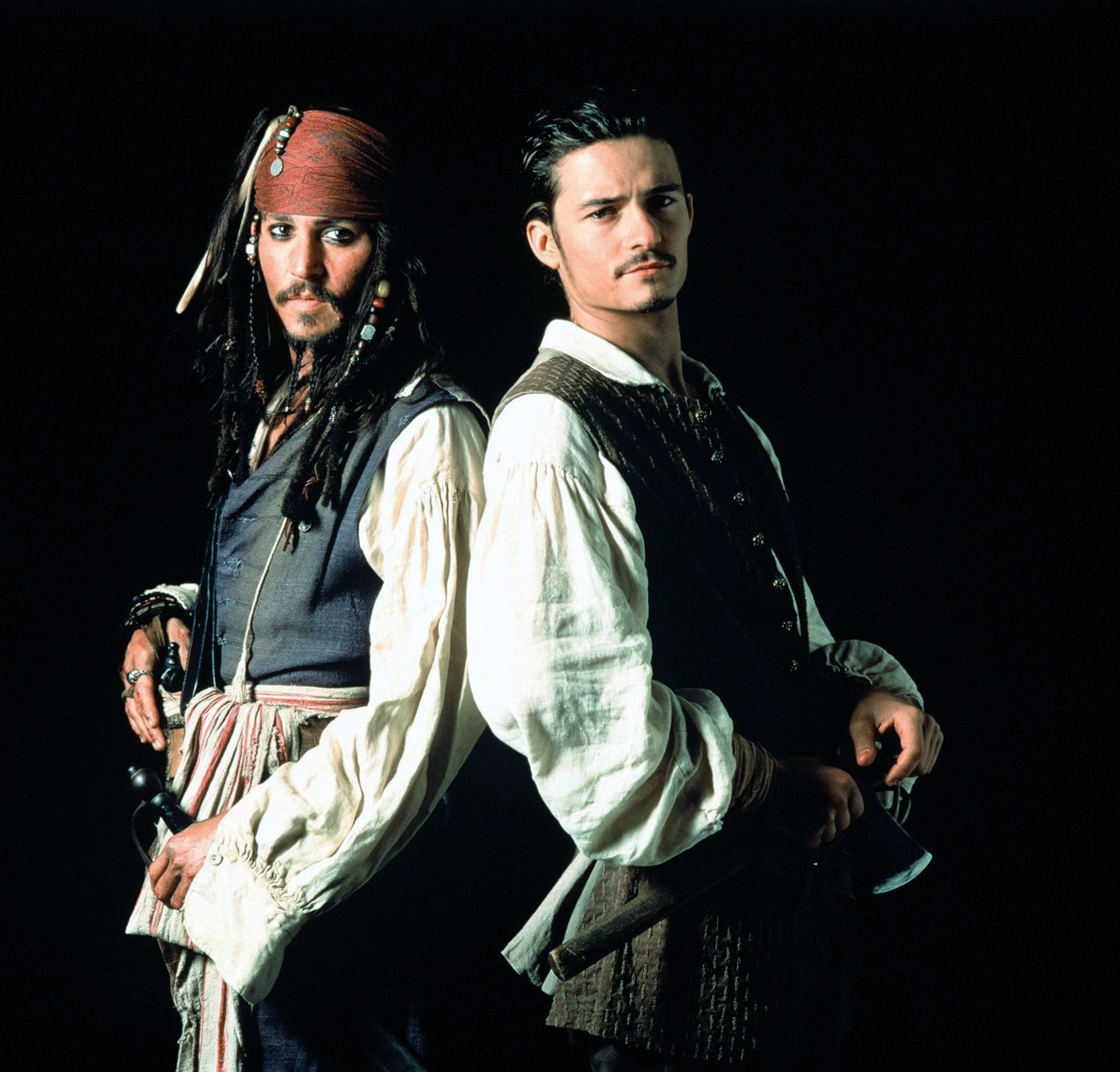 Orlando Bloom and Johnny Depp stand with their backs against each other