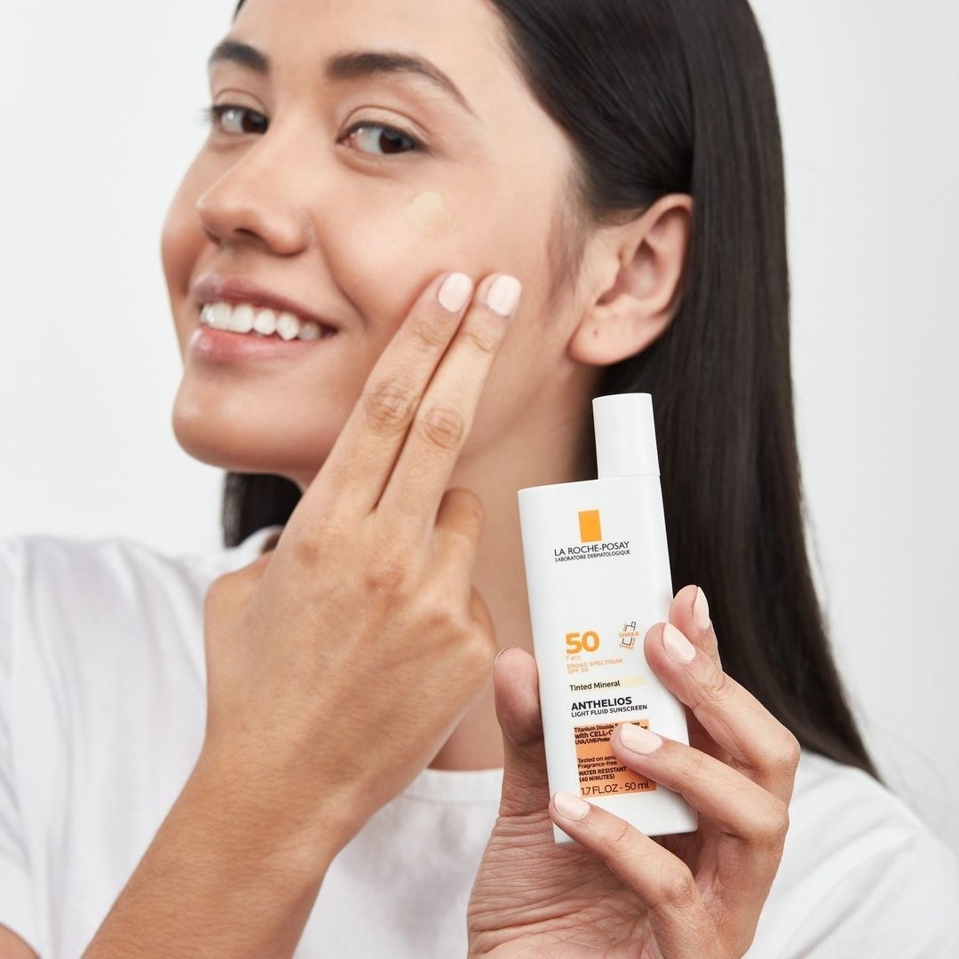 a model holding the bottle of sunscreen while applying it to their face
