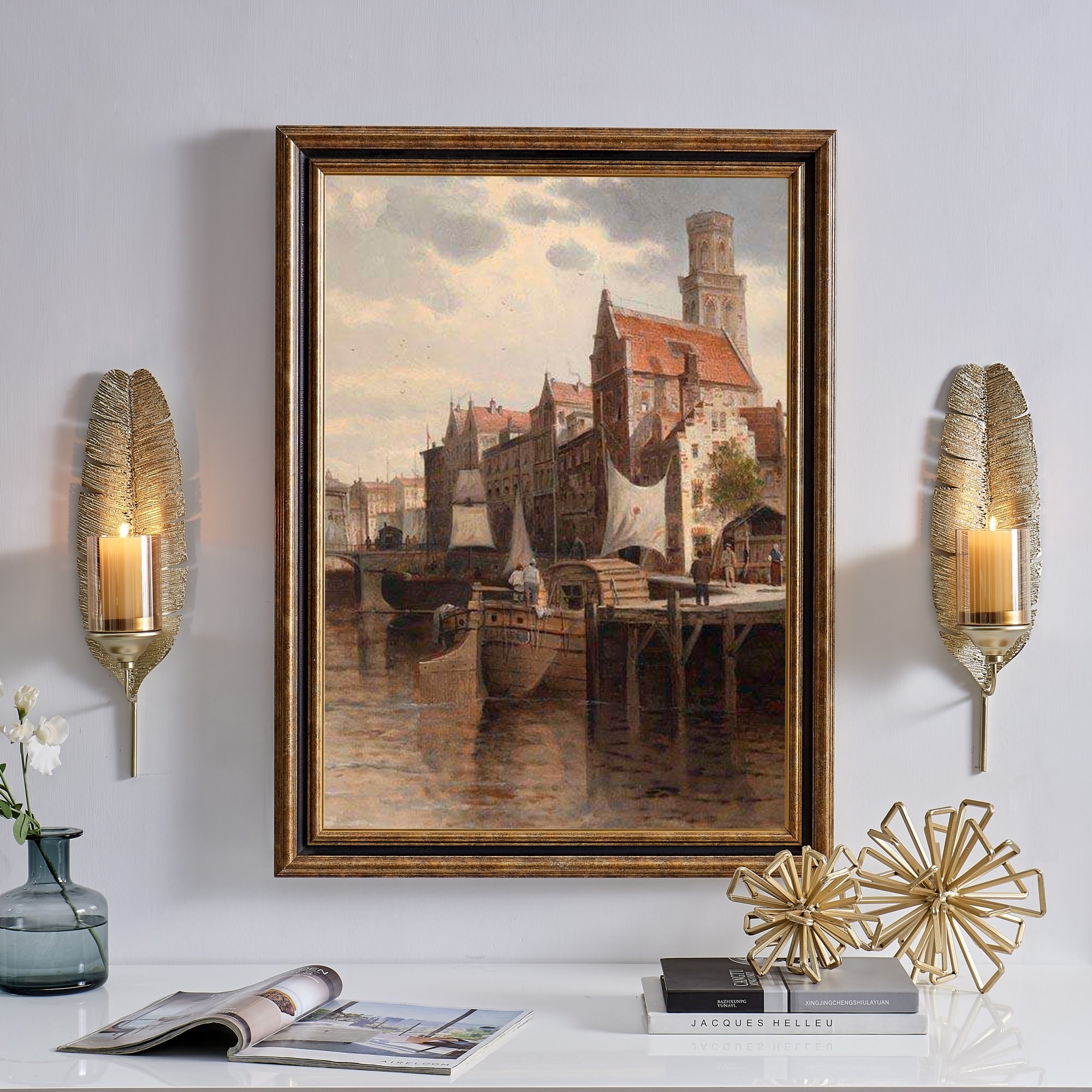 the two gold feather sconces hanging on a wall with a painting in between