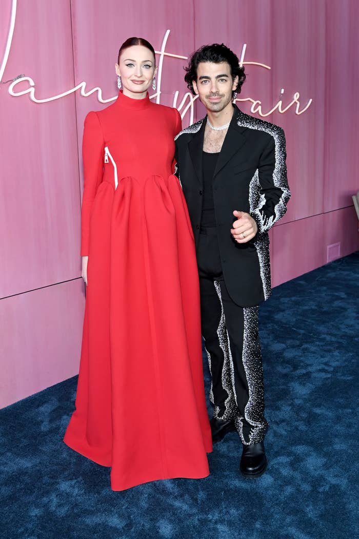 Joe wears a black suit and Sophie wears a long sleeve red gown
