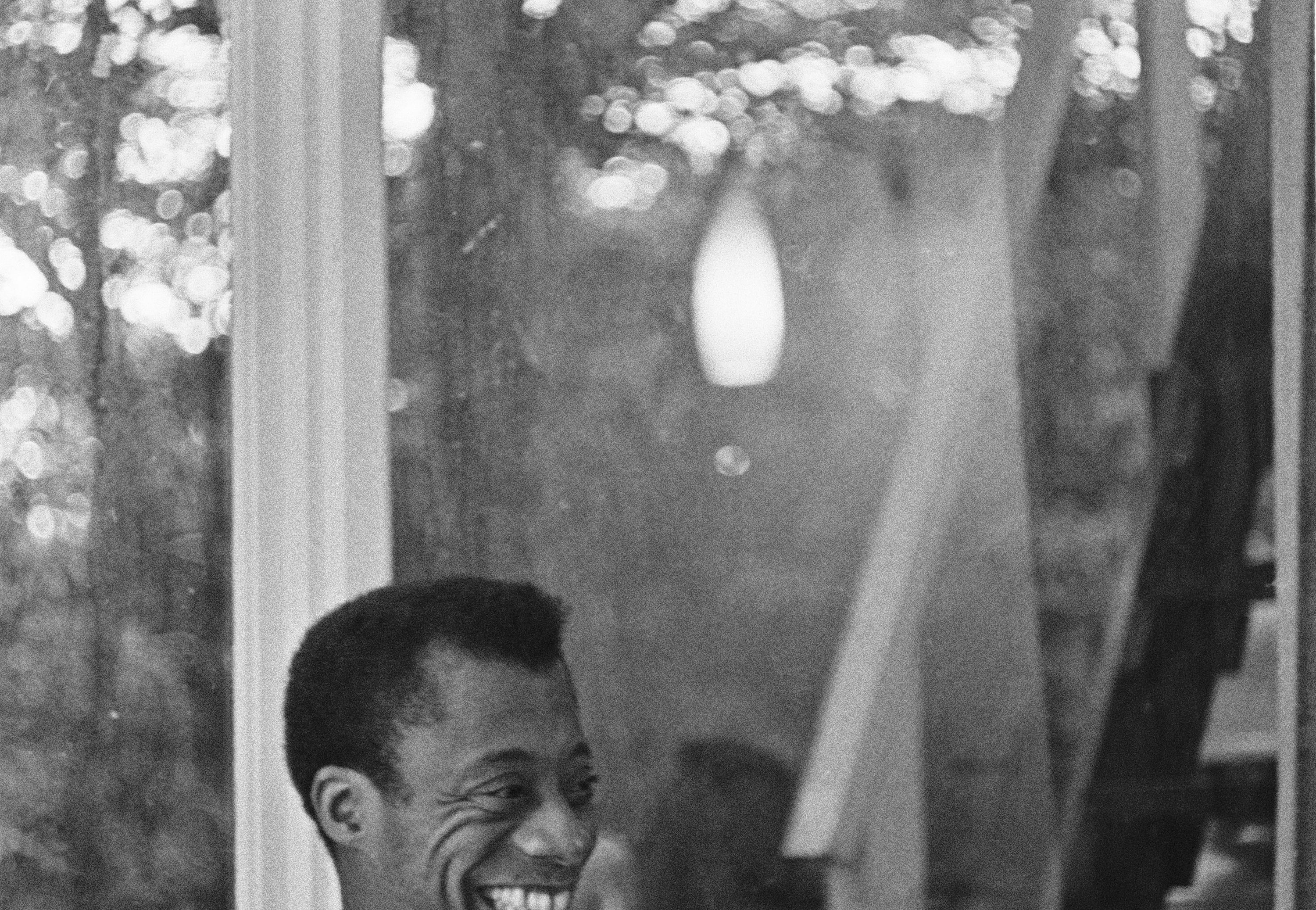 James Baldwin smiling while relaxing on a porch