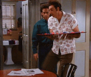 GIF of Kramer kicking newspapers off a round table while holding a board game in a &quot;Seinfeld&quot; episode