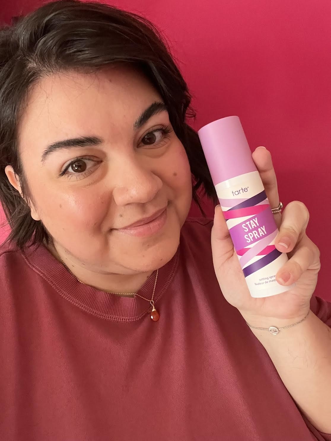 Bianca holding up a bottle of the setting spray next to her face