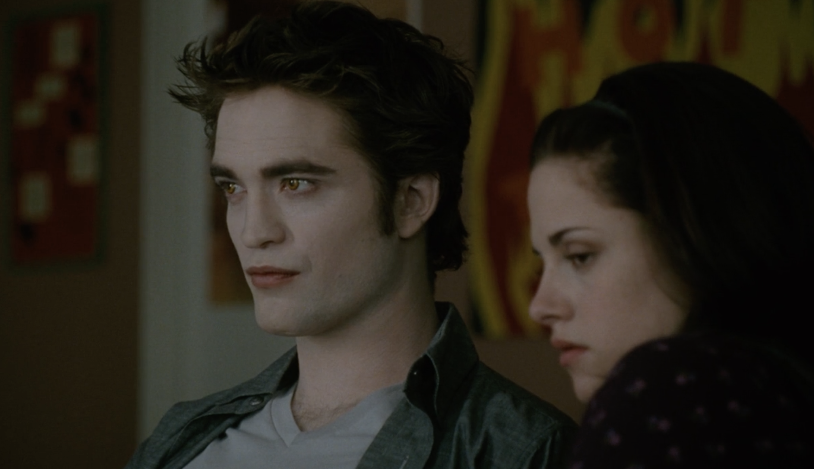 Robert Pattinson, pale with v-neck tee and collar shirt next to Kristen Stewart