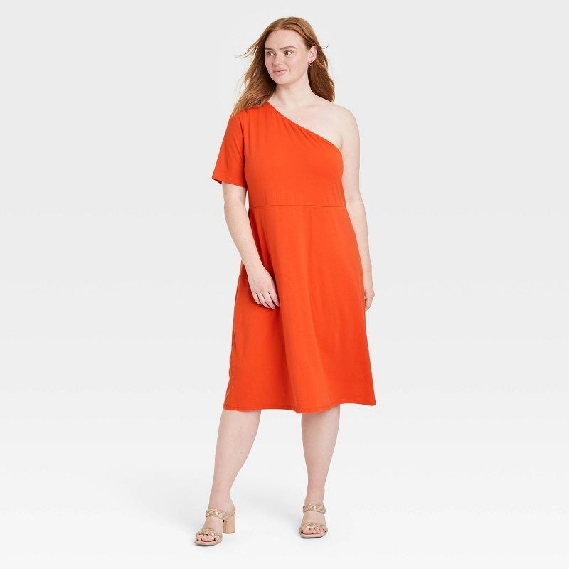 Model wearing light orange dress, goes past the knees