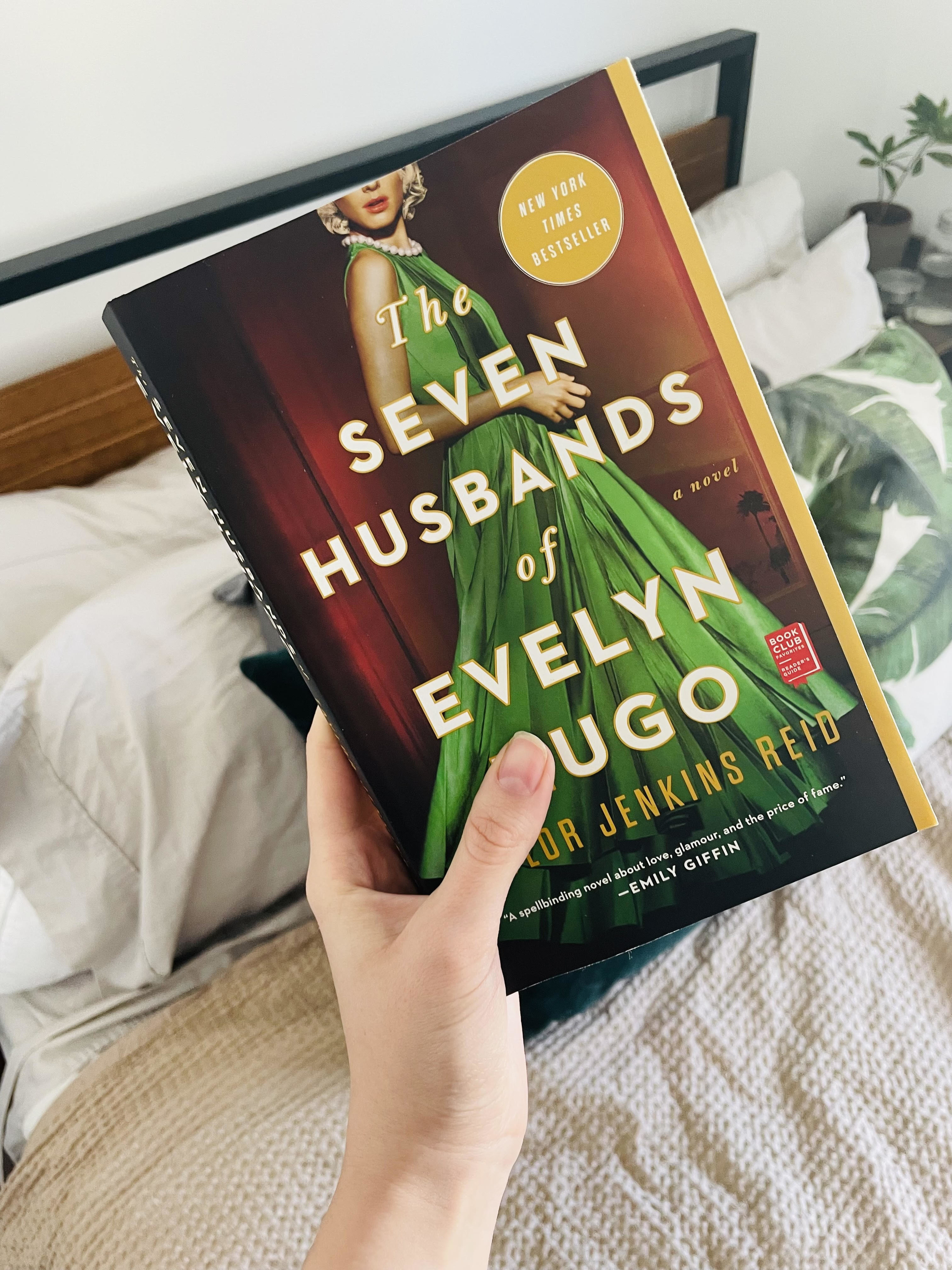 Someone holding &quot;The Seven Husbands of Evelyn Hugo&quot; above a bed
