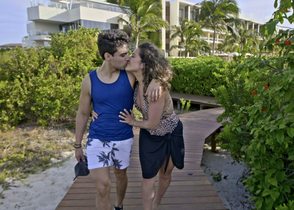 Mallory leans into Sal for a kiss as they walk toward the beach