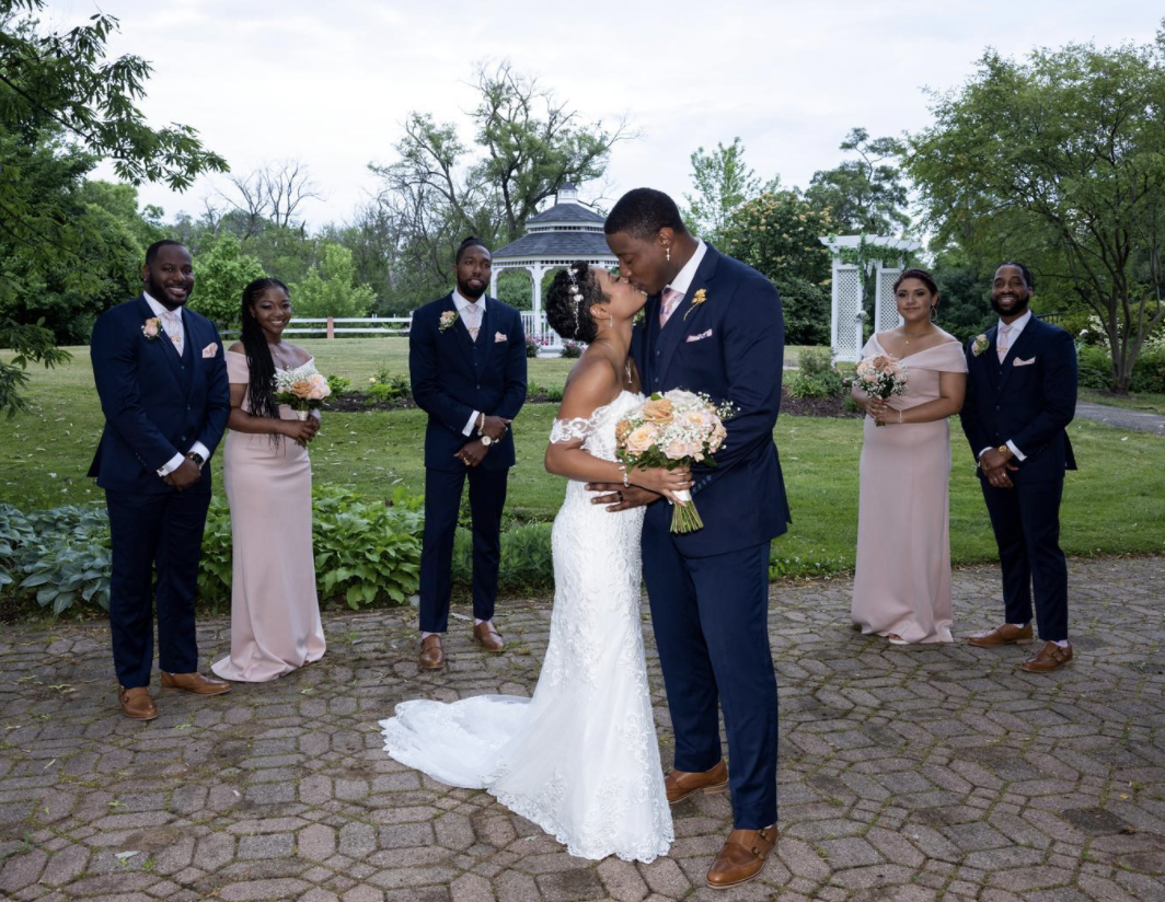 The couple share a kiss after their wedding, surrounded by their bridal party