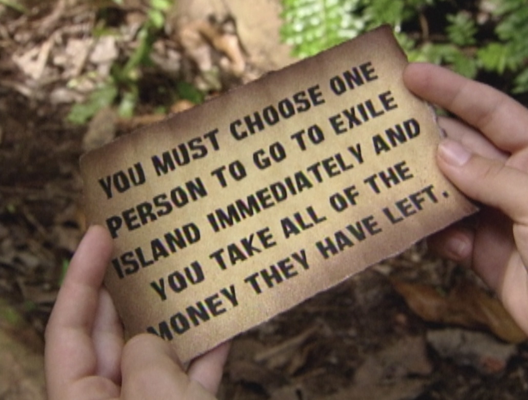piece of parchment reading &quot;you must choose one person to go to exile island immediately and you take all of the money they have left