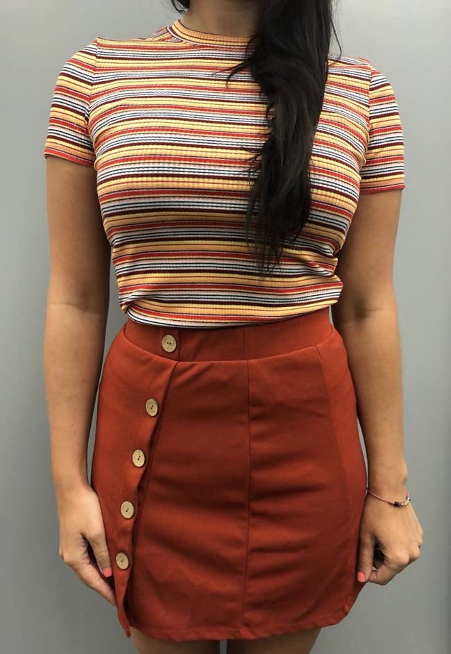 reviewer wearing the tight  multicolor tiny  stripe t-shirt with a brownish  skirt