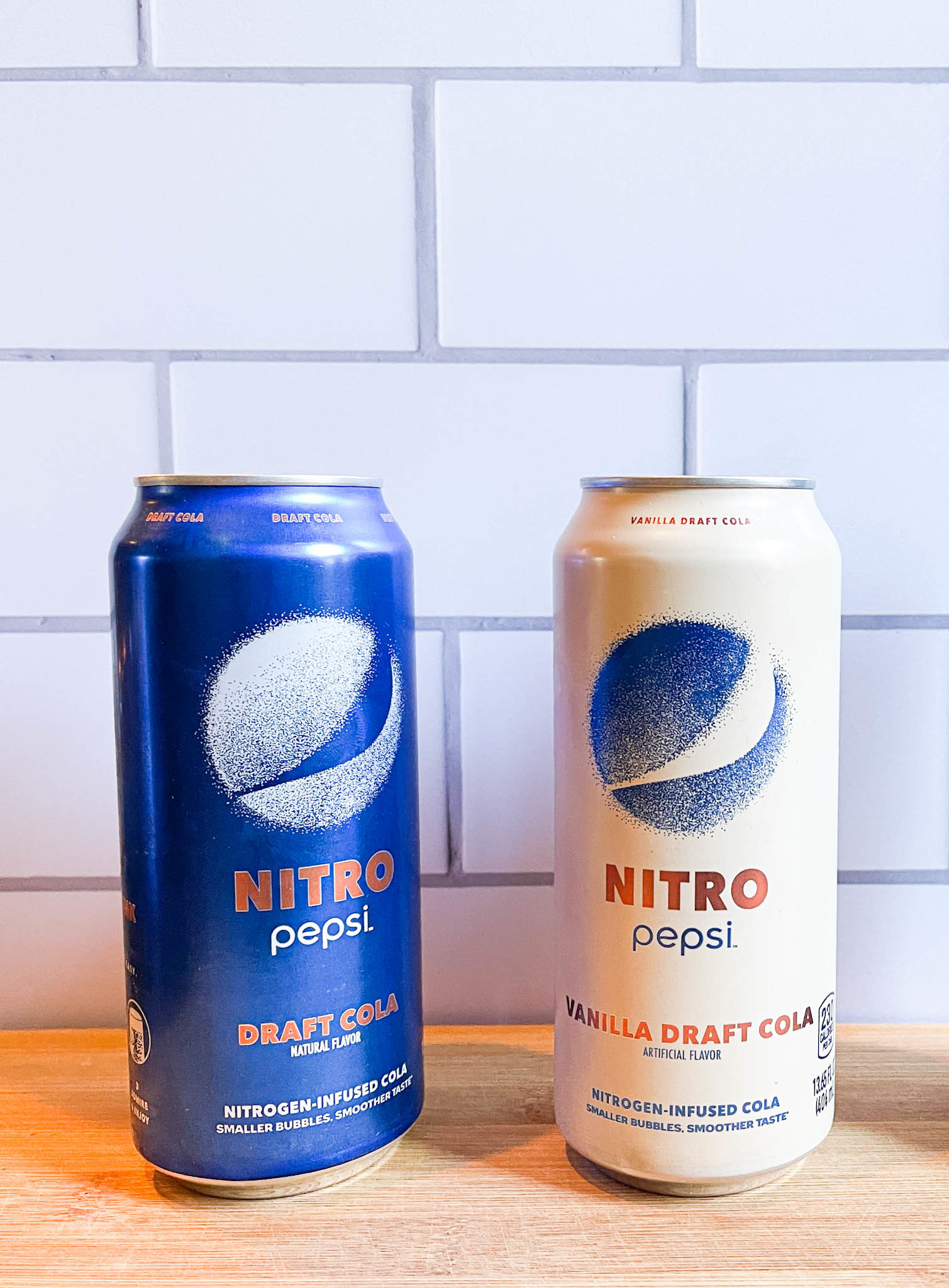 Two cans of Nitro Pepsi next to each other on a cutting board — both regular and vanilla
