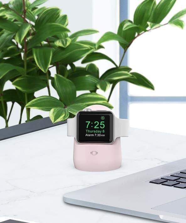 An Apple Watch sitting on the rubber charging dock on top of a desk next to a laptop