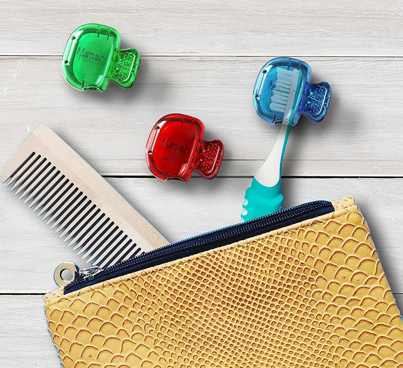 A toothbrush with one of the covers on it and two of the covers and a comb sticking out of a cosmetic bag