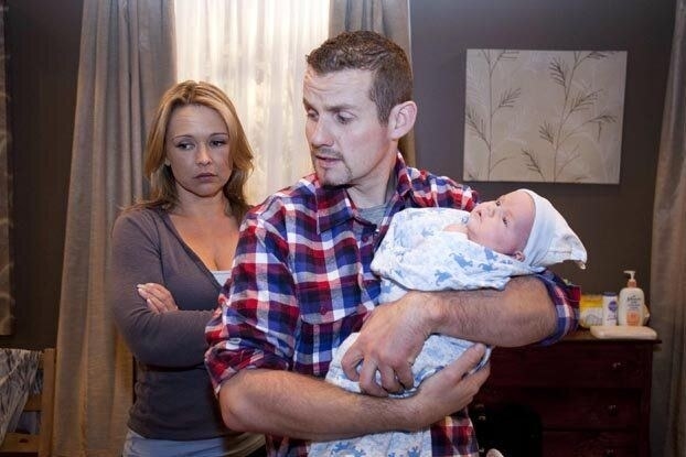 A character from Neighbours called Toadie, he is holding a baby