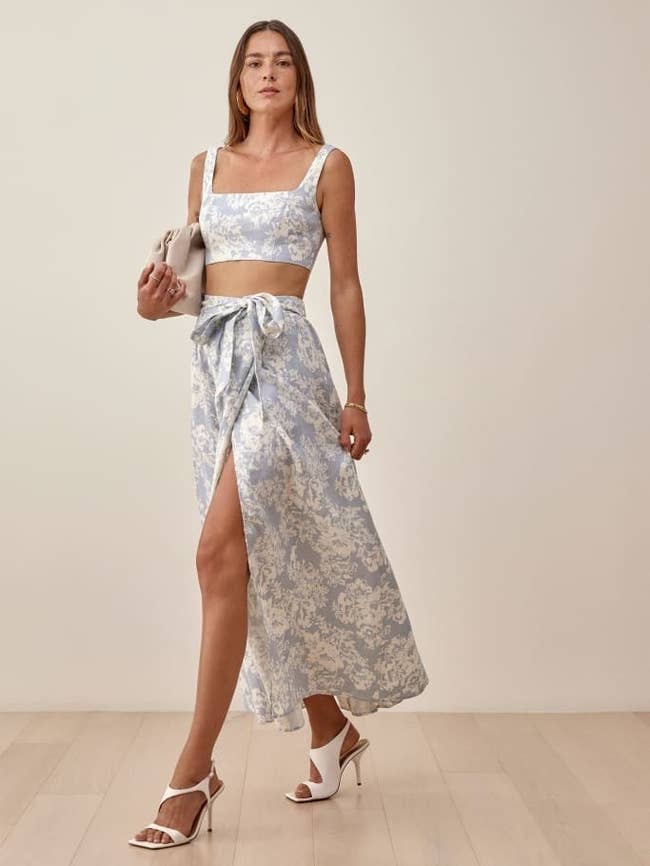 a model wearing the blue floral skirt and top with white heels and matching bag