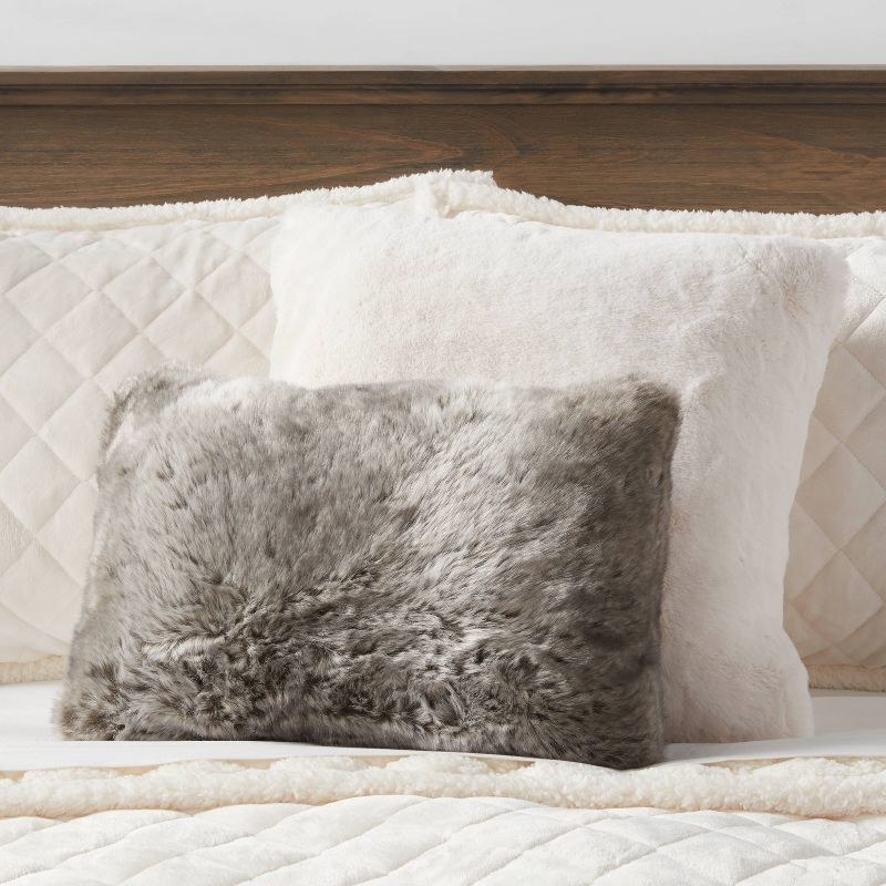 a gray faux fur pillow on a bed
