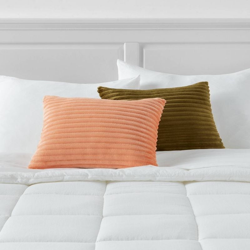 a pink and green textured pillow on a white bed