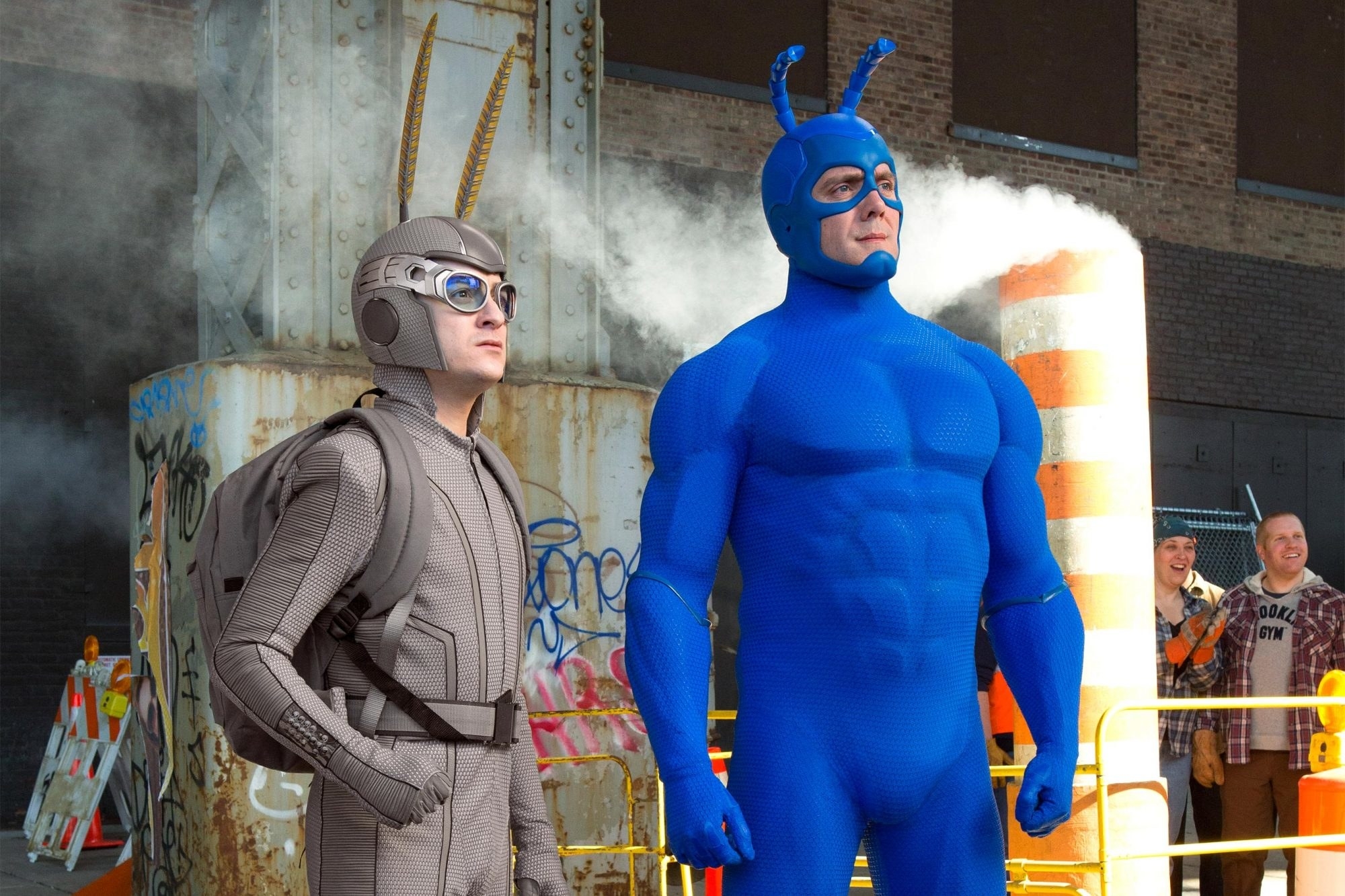 Arthur in his moth suit and the Tick standing on a street looking at something to the right