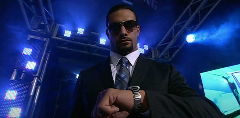 Roman Reigns, in a suit, looks at his watch