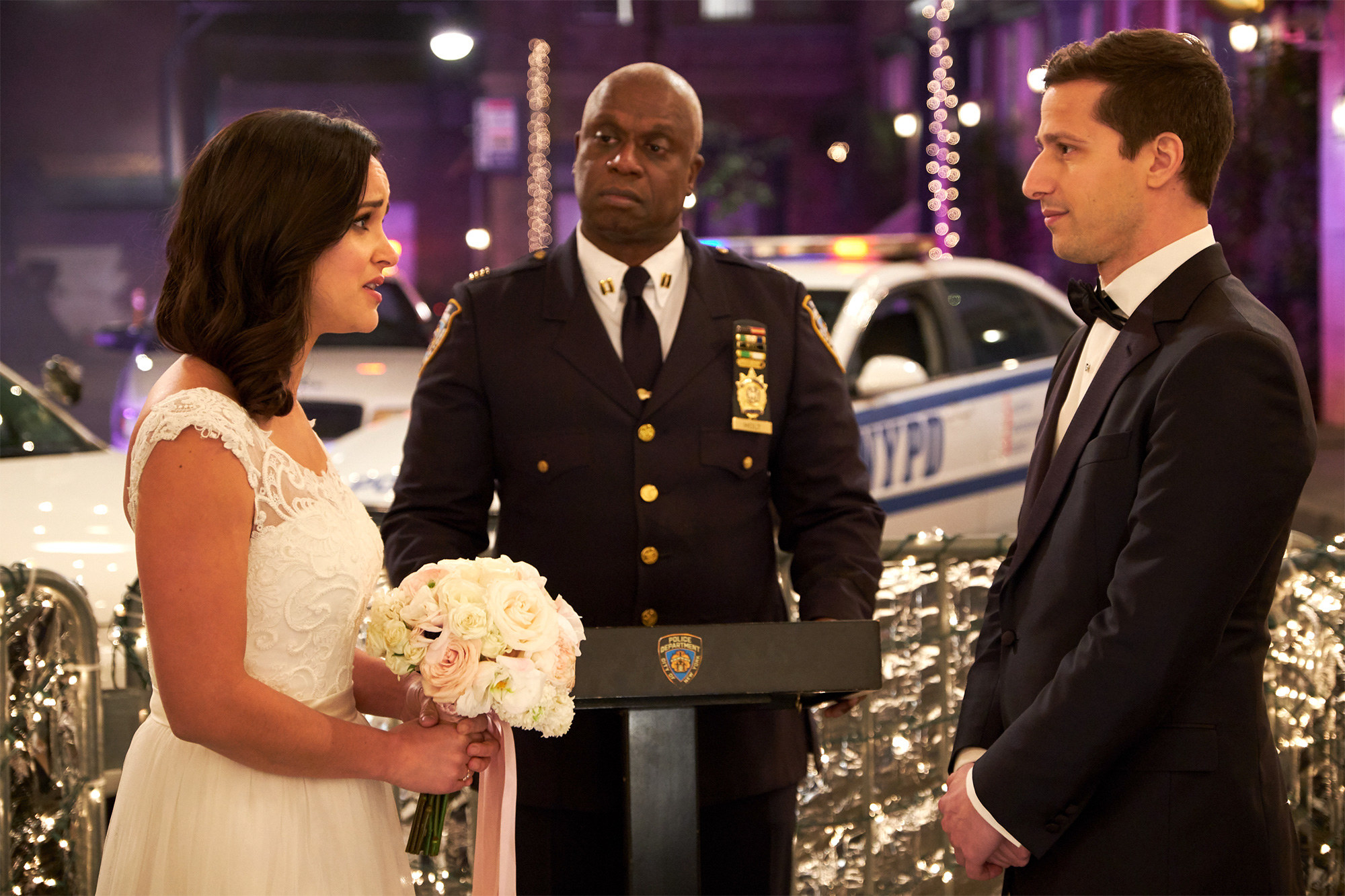 Andy Samberg as Jake Peralta marrying Melissa Fumero as Amy Santiago with Andre Braugher as Captain Holt ordaining in Brooklyn Nine-Nine
