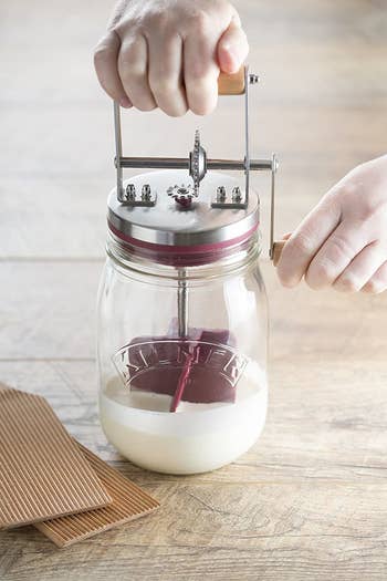 A glass mini butter churner with a lid and a handle for churning the inside spatula